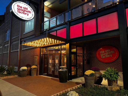 Exterior of The Old Spaghetti Factory restaurant, featuring a lit marquee and colorful flower pots at night.
