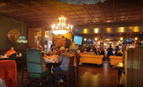 A cozy restaurant interior with patrons dining, ornate decor, and a chandelier illuminating the space.