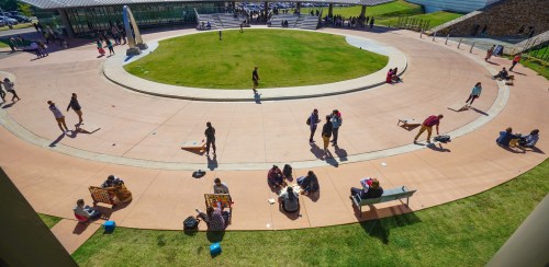 Aerial view of a circular park area with people sitting, walking, and playing games on a sunny day.