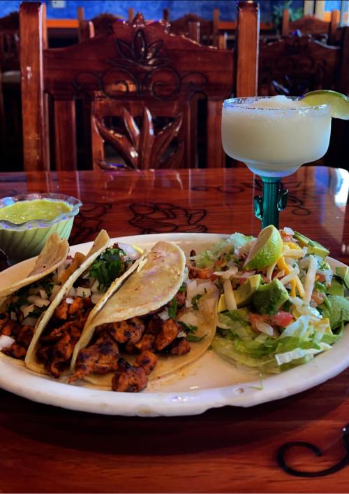 A plate of three tacos with meat, onions, and cilantro, served with a side of salad and a margarita.