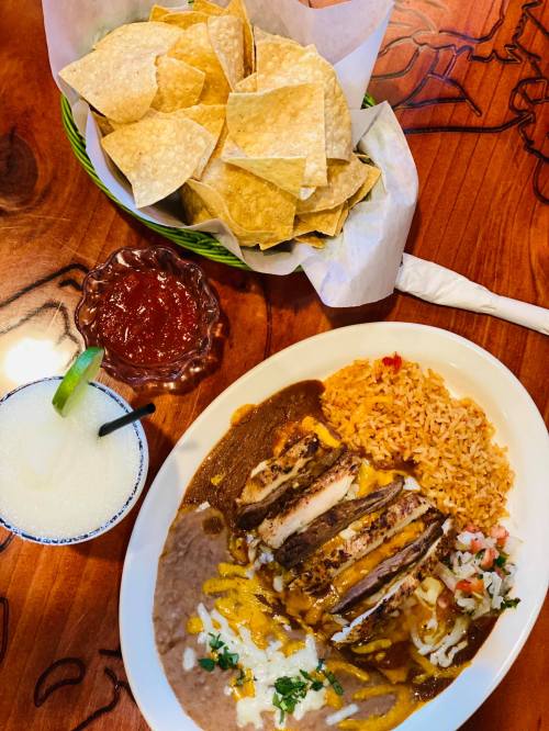 A plate of chicken enchiladas with rice and beans, served with tortilla chips, salsa, and a margarita.