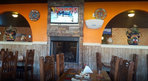 Cozy restaurant interior with wooden tables, colorful decor, a fireplace, and a TV displaying a sports event.