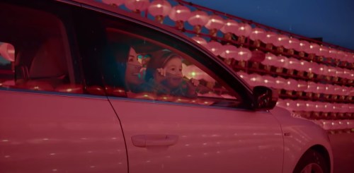 A woman and child smile from inside a car, illuminated by red lanterns in the background.