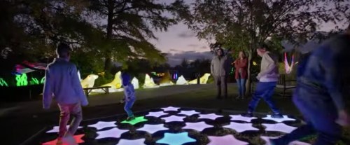 A group of people play on a colorful illuminated star-shaped floor at night, surrounded by glowing decorations.