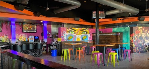 Vibrant bar interior with colorful stools, artistic murals, and a lively atmosphere.