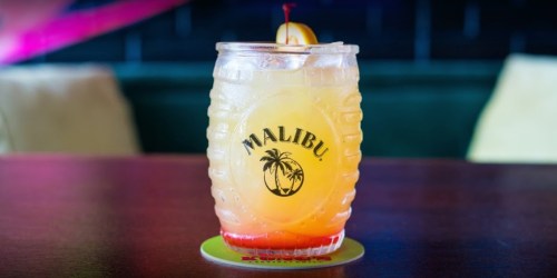 A refreshing cocktail in a glass with a palm tree logo, garnished with a cherry and a slice of fruit.