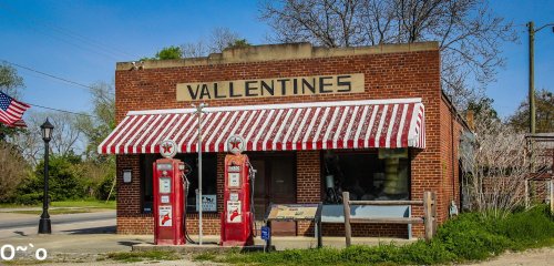Historic brick building with a striped awning, vintage gas pumps, and a sign reading "Vallentine's."