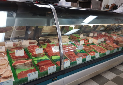 A display case filled with various cuts of meat, labeled and arranged on green trays in a butcher shop.