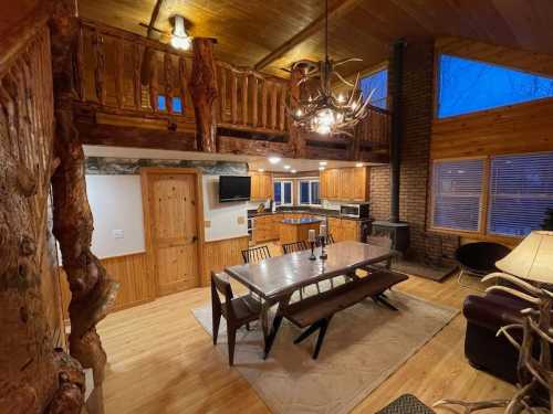 Cozy cabin interior featuring a wooden dining table, rustic decor, and large windows with a view of the evening sky.