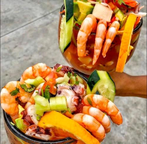 Two large glasses filled with shrimp, octopus, and fresh vegetables, garnished with colorful toppings.