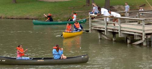 Two canoes on a lake with people in life jackets, while others fish from a wooden dock nearby.