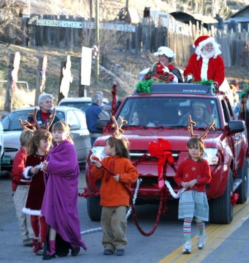 A festive parade scene with children in holiday attire and Santa on a decorated red truck.