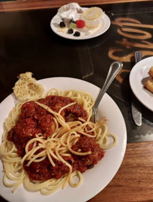 A plate of spaghetti with meatballs and marinara sauce, accompanied by a side of garlic bread and a dessert plate.