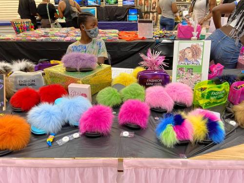 A colorful display of fluffy accessories on a table, with a child wearing a mask in the background.
