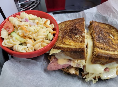 A toasted sandwich filled with meat and cheese, served with a side of pasta salad in a red bowl.