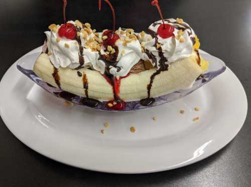 A banana split topped with whipped cream, chocolate syrup, nuts, and cherries, served in a clear dish.