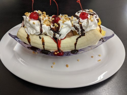 A banana split topped with whipped cream, chocolate syrup, nuts, and cherries, served in a clear dish.