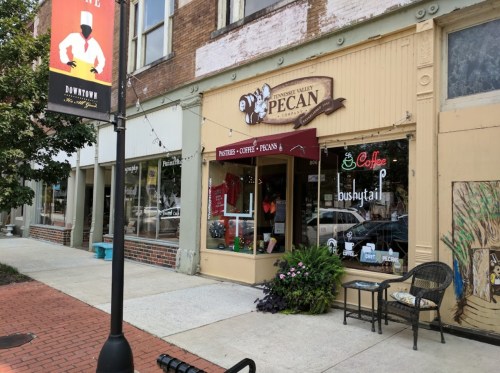 A storefront labeled "Sweet Valley Pecan" featuring coffee and pecan treats, with outdoor seating and a vibrant facade.