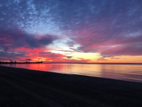 A vibrant sunset over calm waters, with colorful clouds reflecting on the surface and a silhouette of a shoreline.