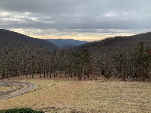 A scenic view of a mountainous landscape with bare trees and a winding dirt road under a cloudy sky.