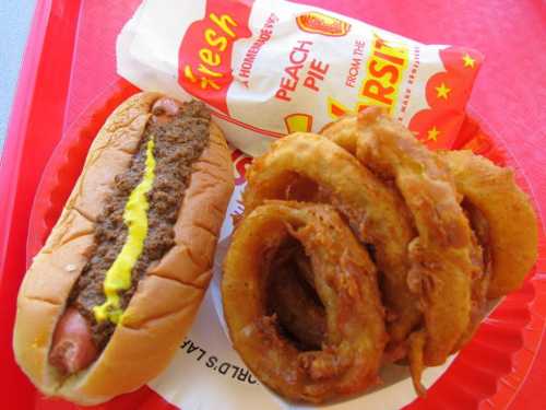 A hot dog with mustard, a peach pie, and crispy onion rings on a red tray.