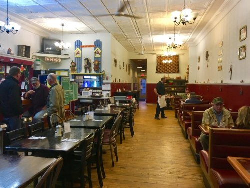 A cozy restaurant interior with wooden tables, chairs, and patrons enjoying their meals in a warm, inviting atmosphere.