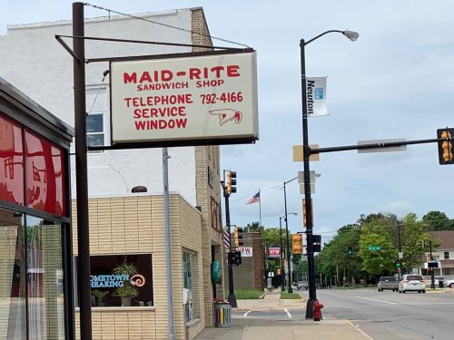Sign for Maid-Rite Sandwich Shop with a service window, located on a street with traffic lights and nearby buildings.