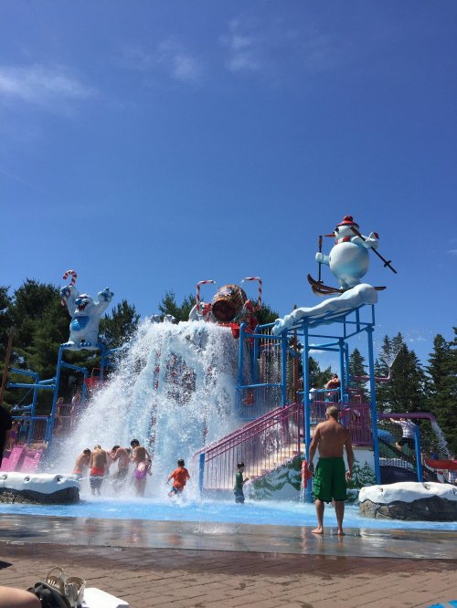 A water park with a large slide, kids playing in the splash area, and whimsical snowman decorations under a clear blue sky.