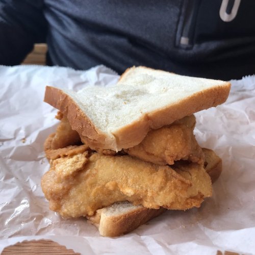 A sandwich with two pieces of fried chicken between slices of white bread, resting on crumpled paper.