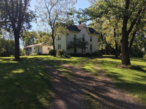 A white house surrounded by trees and a grassy lawn, with a gravel driveway leading up to it.