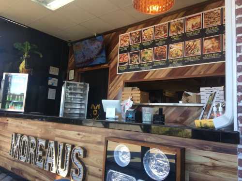 Interior of a restaurant with a wooden counter, menu on the wall, and a display fridge.