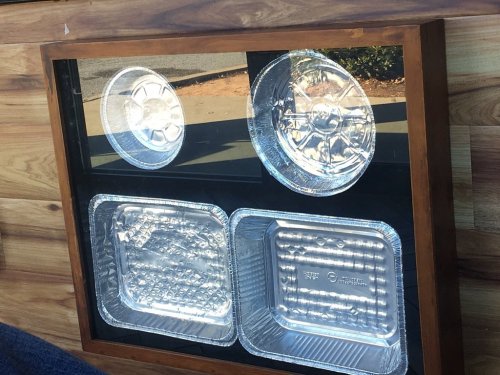 A wooden display case featuring various aluminum food trays and lids arranged neatly inside.