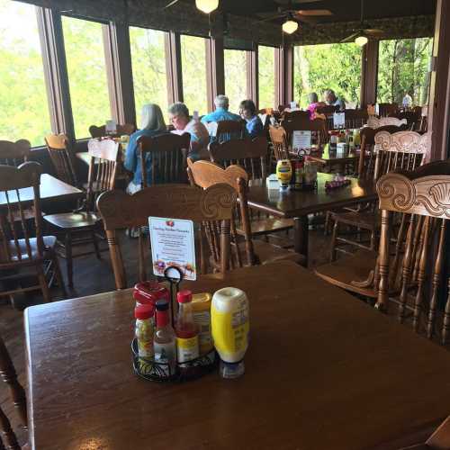 A cozy restaurant interior with wooden tables, condiments on the table, and patrons enjoying their meals by large windows.