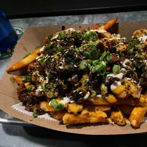 A tray of loaded fries topped with cheese, green onions, and a savory sauce, served with a blue drink in the background.