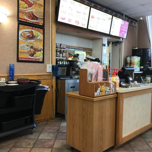 A diner interior featuring a counter with a menu board, condiments, and seating area.