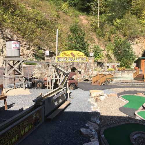 A scenic view of Smoky Hole Caverns with mini-golf, stone structures, and lush greenery in the background.