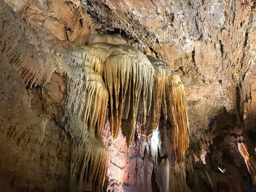 Stalactites hang from a rocky cave ceiling, illuminated by soft lighting, showcasing natural formations.