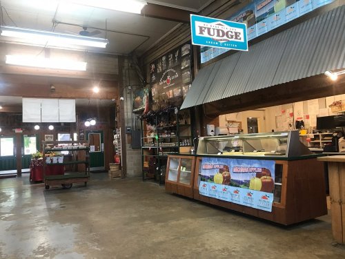 Interior of a rustic shop featuring a fudge counter, display cases, and wooden beams, with various products on shelves.