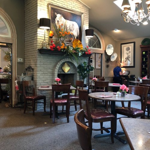 Cozy restaurant interior with wooden tables, chairs, a stone fireplace, and floral decor on the walls.