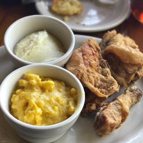 A plate with fried chicken, mashed potatoes, and macaroni and cheese in bowls, with a biscuit in the background.
