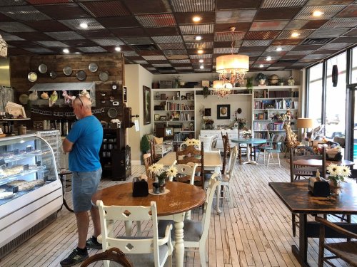 A cozy café interior with wooden tables, bookshelves, and a display case, featuring a man standing near the counter.