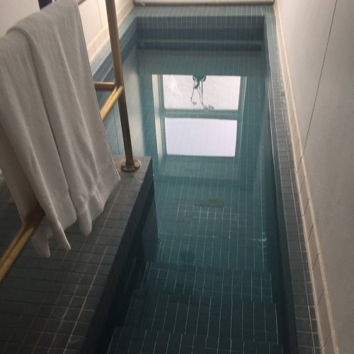 A narrow indoor pool with clear water, tiled walls, and a towel hanging on a railing nearby.