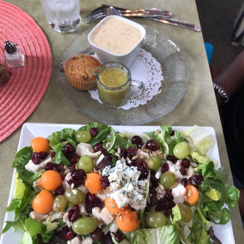 A colorful salad with greens, chicken, grapes, melon, and blue cheese, served with a muffin and soup on the side.