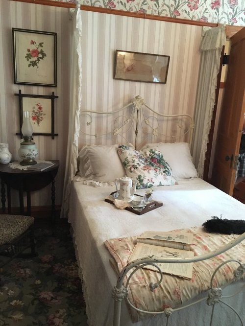 A cozy vintage bedroom with a floral bedspread, a small table, and decorative wall art.