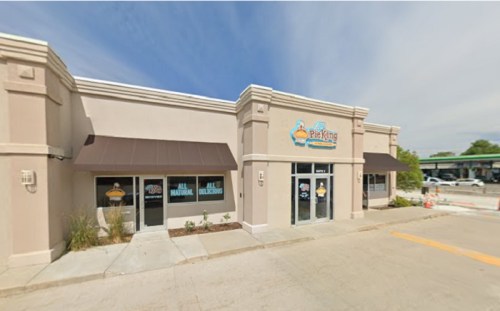 Exterior view of a Pie King restaurant with a light-colored facade and large windows, featuring a blue and orange sign.