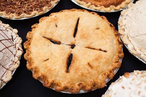 A freshly baked pie with a golden crust and slits on top, surrounded by various other pies on a black surface.