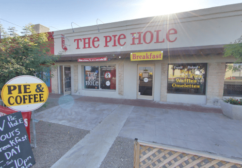 Exterior of "The Pie Hole" restaurant, featuring a sign for breakfast, pie, and coffee. Bright sunlight in the background.
