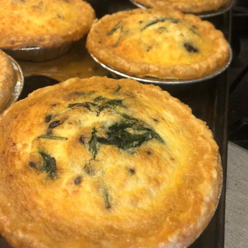 Freshly baked quiches with golden crusts and green spinach visible on top, arranged on a baking tray.
