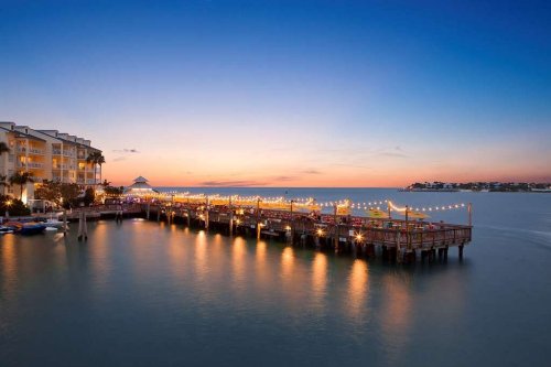 A serene waterfront scene at sunset, featuring a pier adorned with lights and calm waters reflecting the colorful sky.