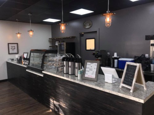 A modern café interior featuring a counter with a display case, coffee equipment, and stylish pendant lighting.